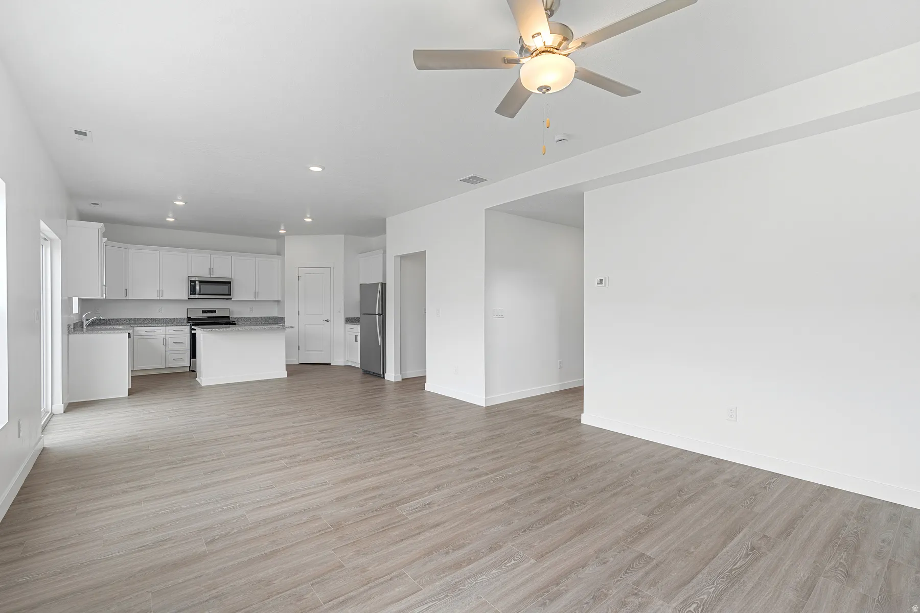 Unfurnished living room featuring light wood-style floors, ceiling fan, and recessed lighting