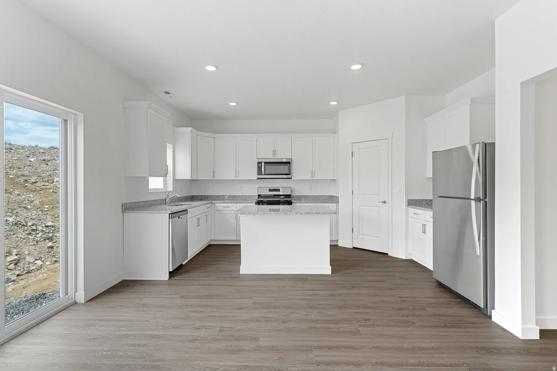 Kitchen featuring stainless steel appliances, a kitchen island, white cabinetry, light stone counters, and recessed lighting