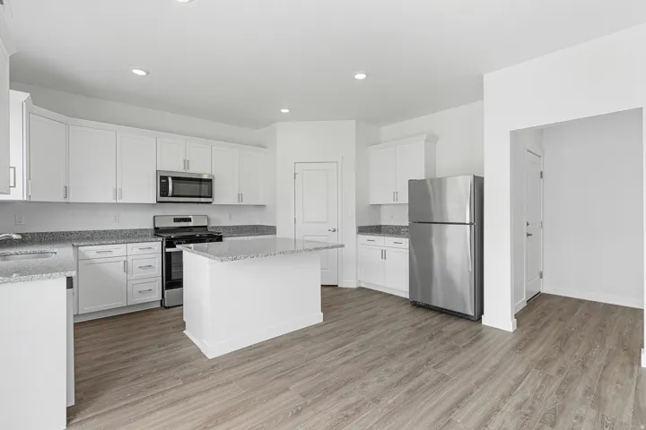 Kitchen featuring stainless steel appliances, light stone counters, light wood-type flooring, white cabinets, and a center island
