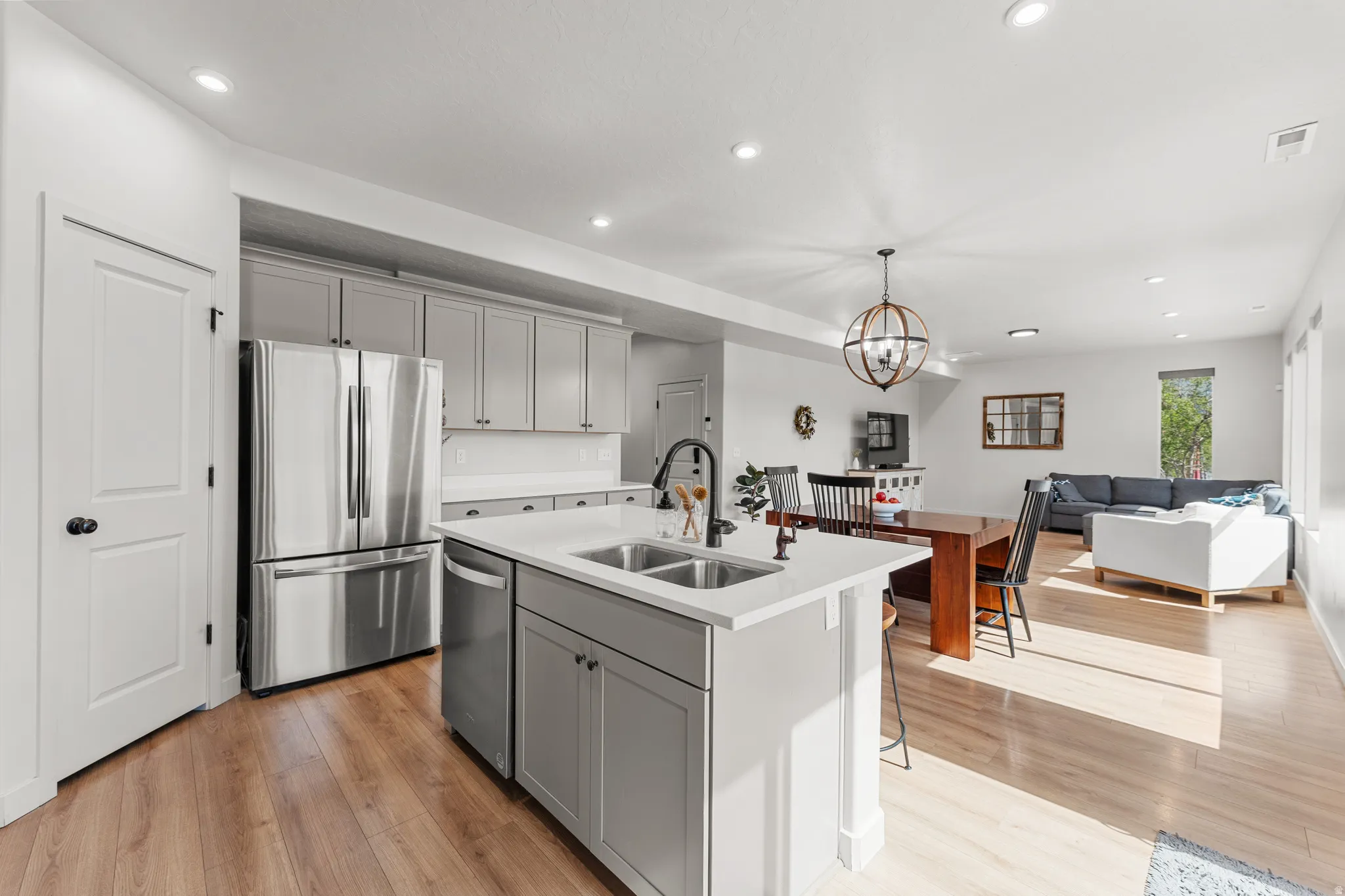 Kitchen with stainless steel appliances, a chandelier, open floor plan, an island with sink, and gray cabinets