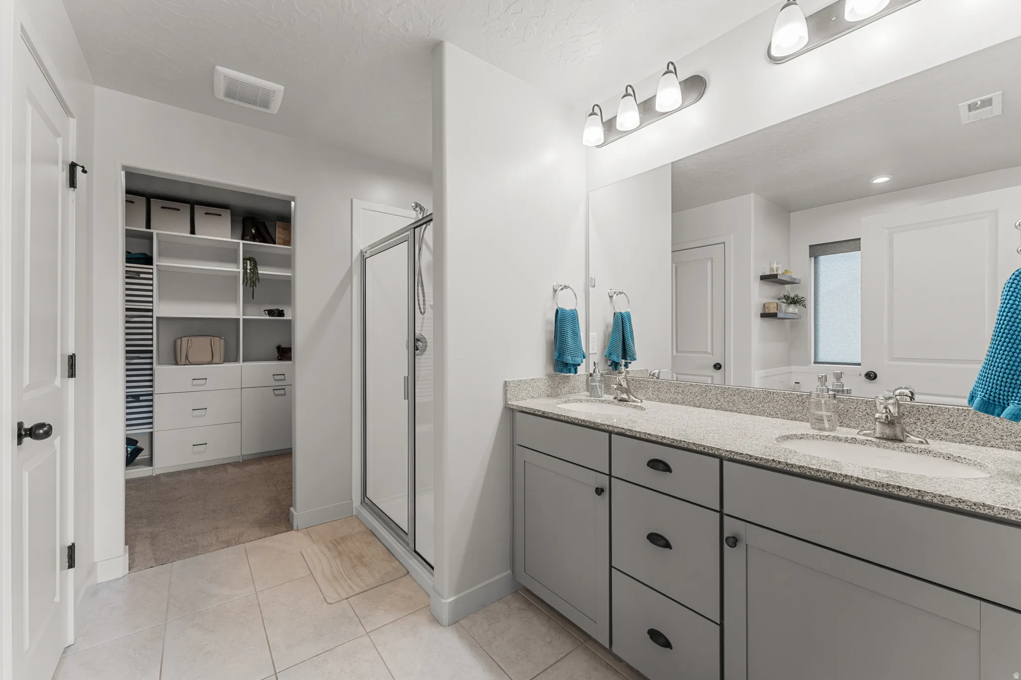Full bathroom featuring double vanity, a spacious closet, a stall shower, light tile patterned flooring, and a textured ceiling