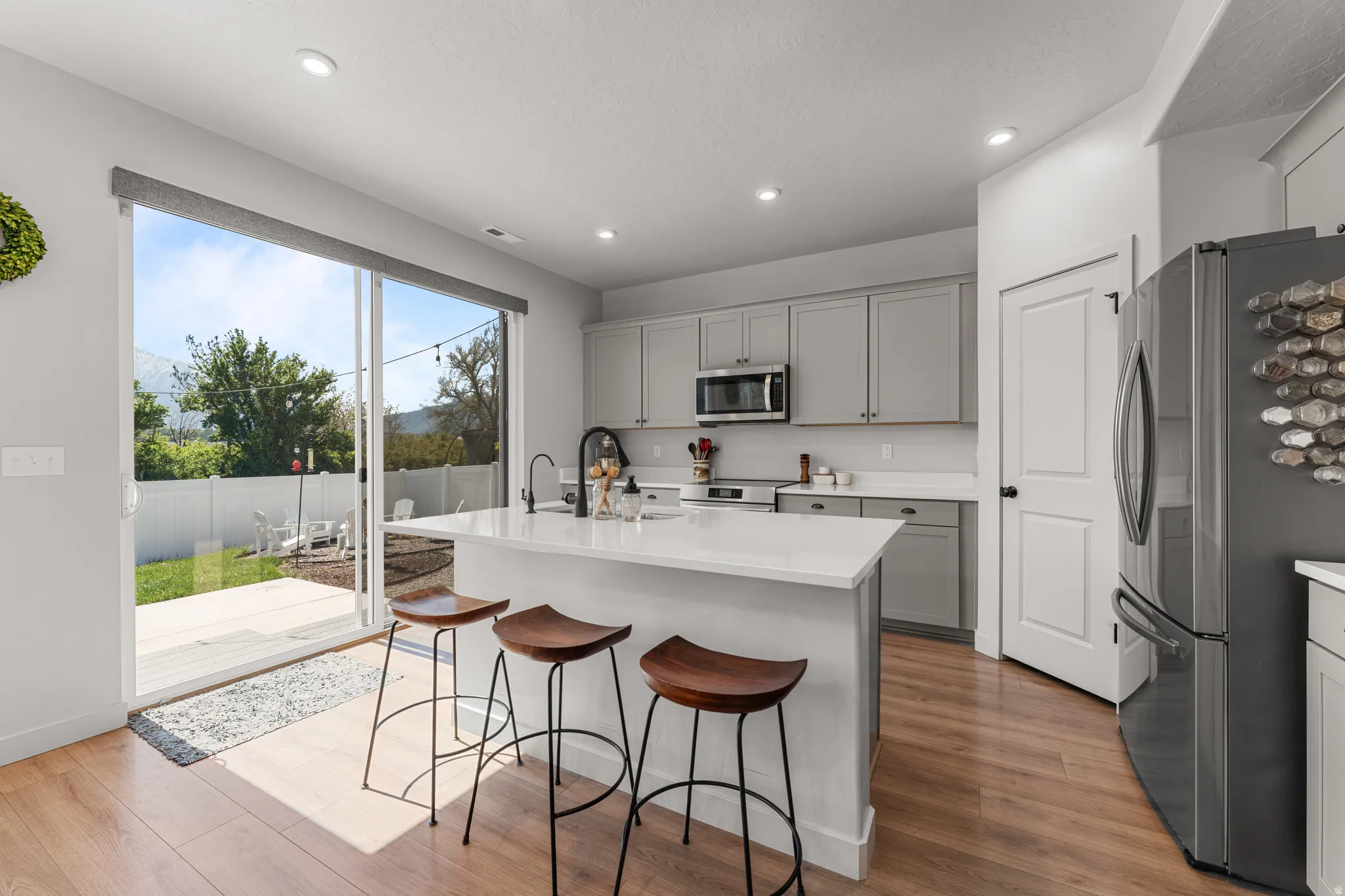 Kitchen with gray cabinetry, stainless steel appliances, a kitchen island with sink, a breakfast bar, and light wood finished floors