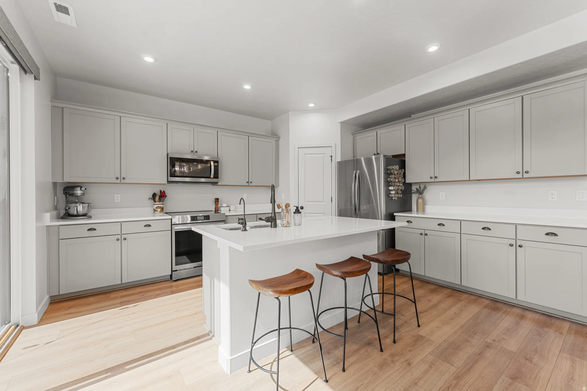 Kitchen featuring gray cabinetry, stainless steel appliances, light wood-type flooring, a kitchen bar, and recessed lighting