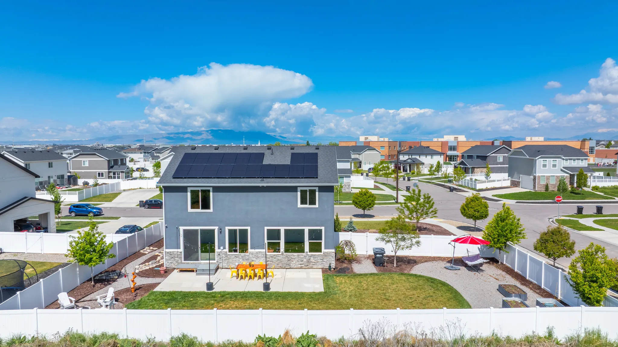 Back of property featuring roof mounted solar panels, a residential view, stone siding, stucco siding, and a fenced backyard
