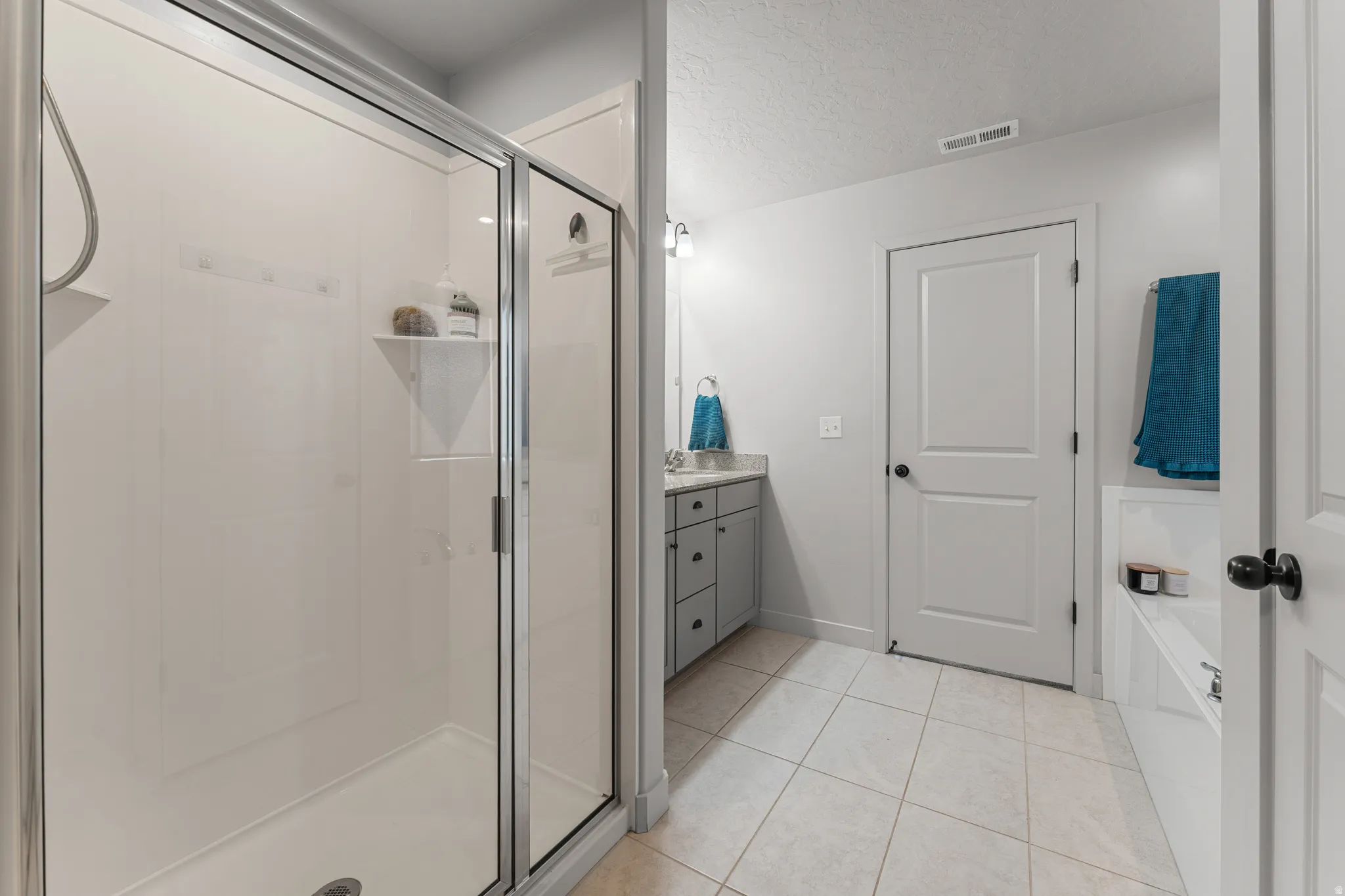 Bathroom with vanity, a shower stall, light tile patterned floors, and a textured ceiling