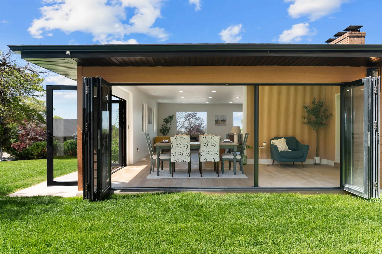 Expansive bi-fold glass doors open to a rear patio and a verdant lawn