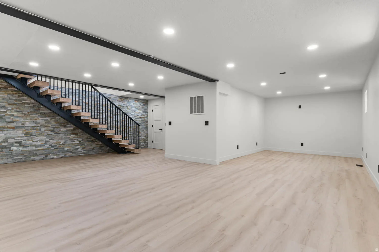 Basement featuring light wood finished floors, an accent wall, and recessed lighting