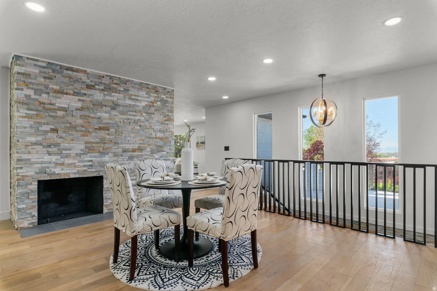 Dining space with light wood-style flooring, a chandelier, a stone fireplace, and a textured ceiling