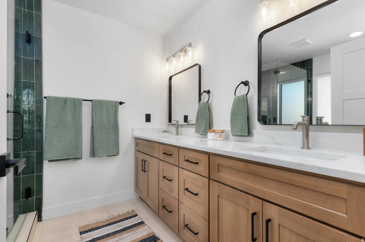 Dual vanity featuring light wood-finish cabinetry with black hardware, white countertops, and integrated sinks