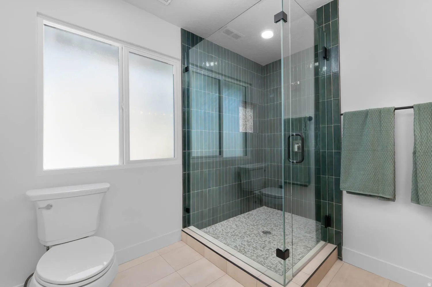 Glass-enclosed shower with vertical teal tile surround and pebble tile flooring