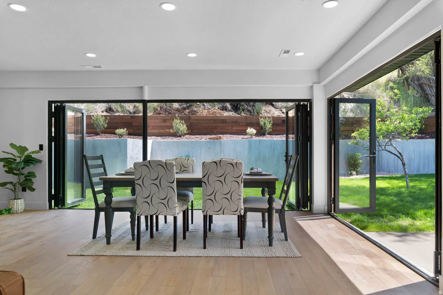 Expansive glass bi-fold doors open to a private outdoor area featuring a mature tree and landscaped terracing