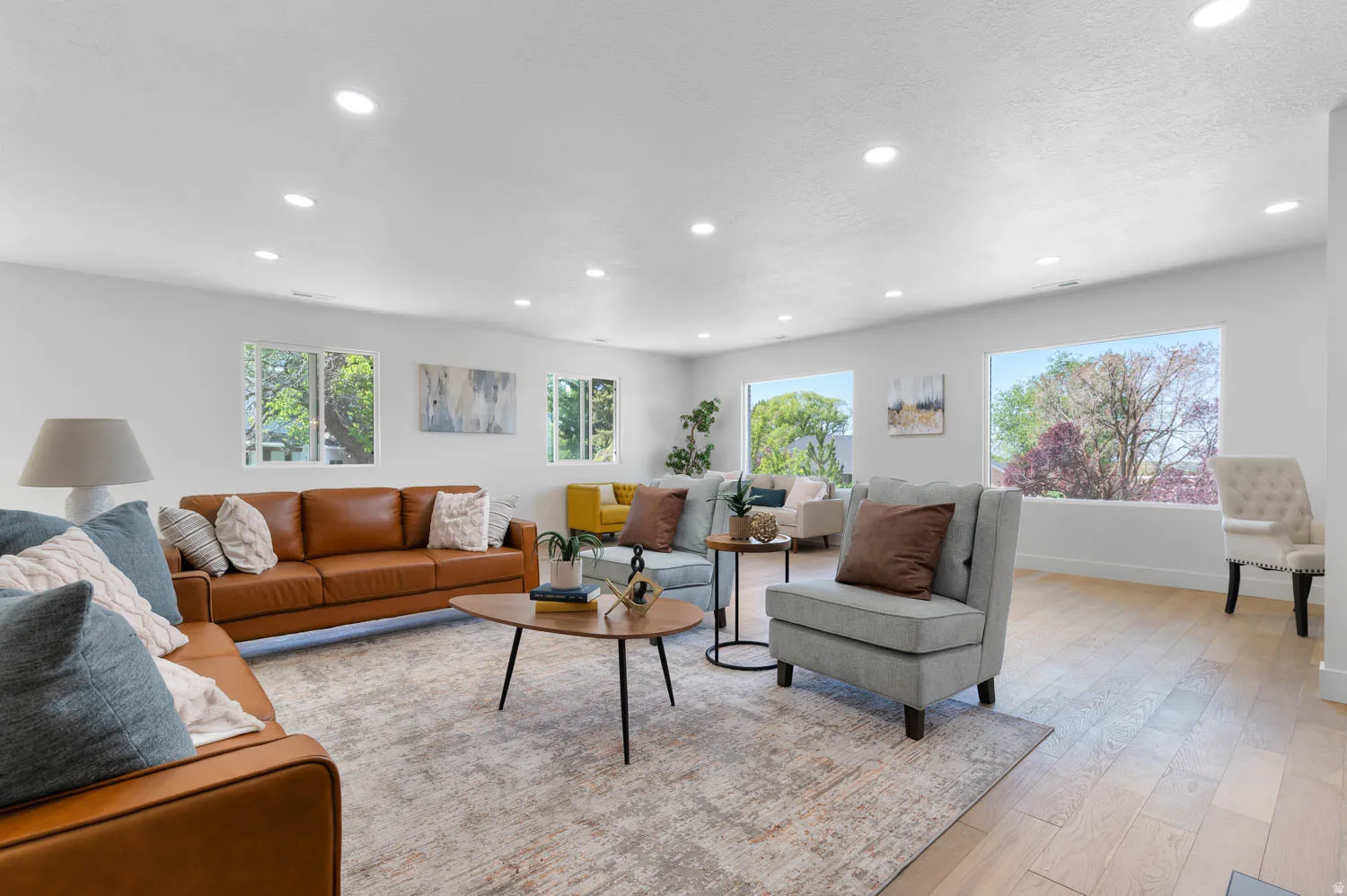 Spacious living area featuring light wood-finish flooring, numerous recessed ceiling lights, and multiple large windows