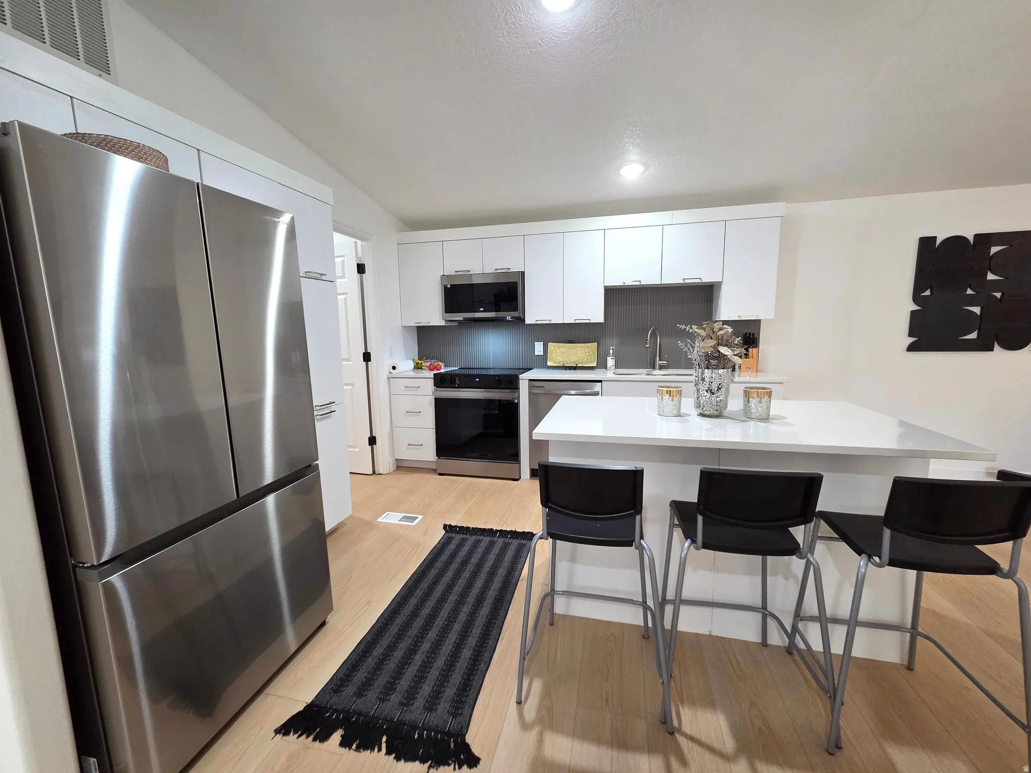 Kitchen featuring stainless steel appliances, white cabinetry, a kitchen island, a breakfast bar, and light wood-type flooring