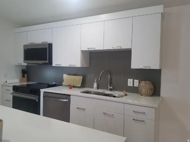 Kitchen featuring white cabinets, stainless steel appliances, light stone countertops, and decorative backsplash