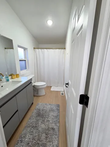 Bathroom with vanity, light wood finished floors, curtained shower, and vaulted ceiling