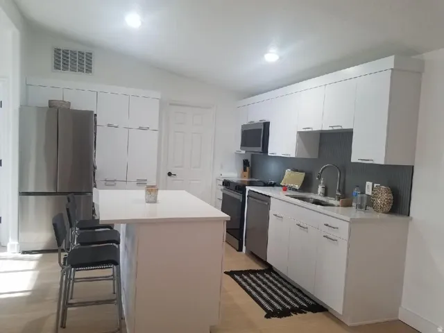 Kitchen featuring a kitchen bar, white cabinetry, a center island, stainless steel appliances, and decorative backsplash