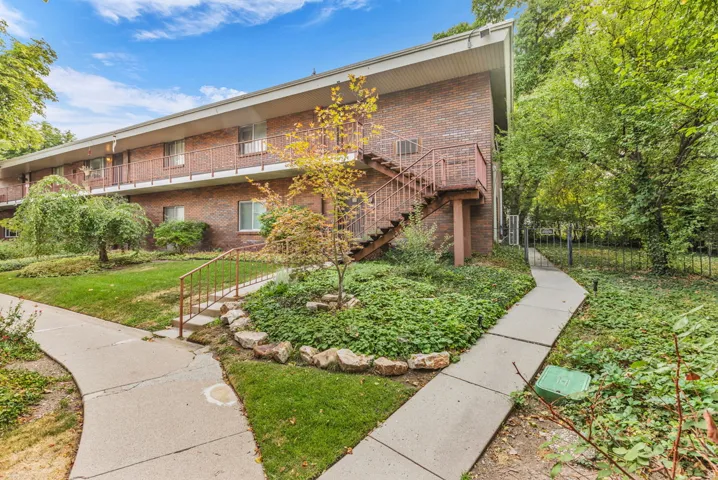 Brick multi-unit residence with mature landscaping, manicured lawn, and established shade trees