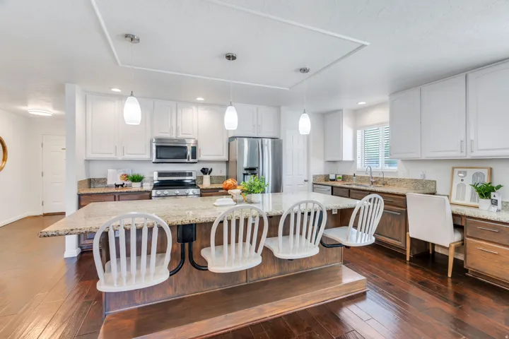 Dual tone kitchen featuring a kitchen island, light stone counters, stainless steel appliances, two tone cabinetry, and dark wood floors
