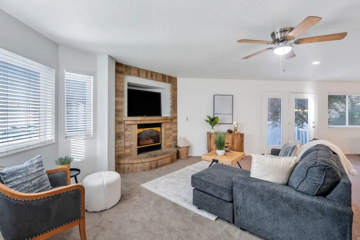 Carpeted living room featuring a ceiling fan and a brick fireplace