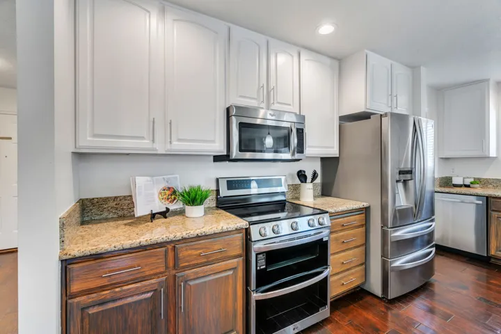 Kitchen featuring stainless steel appliances, white cabinetry, light stone countertops, dark wood finished floors, and recessed lighting