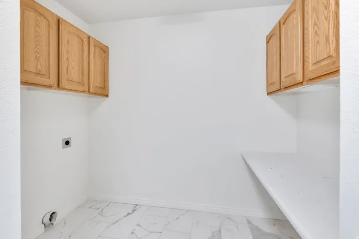 Laundry area with hookup for an electric dryer, cabinet space, and light marble finish flooring