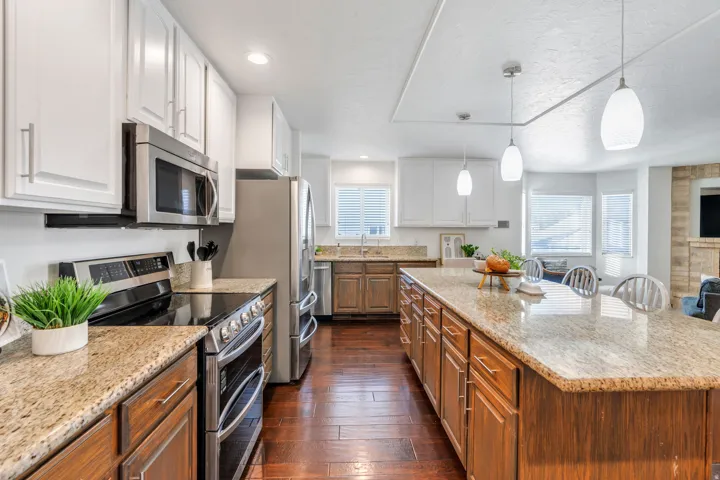 Two tone kitchen with stainless steel appliances, light stone countertops, dual tone cabinets, dark wood floors, and a kitchen island