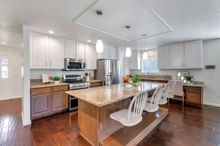 Kitchen with light stone counters, stainless steel appliances, dual tone cabinets, dark wood flooring, and a kitchen breakfast bar