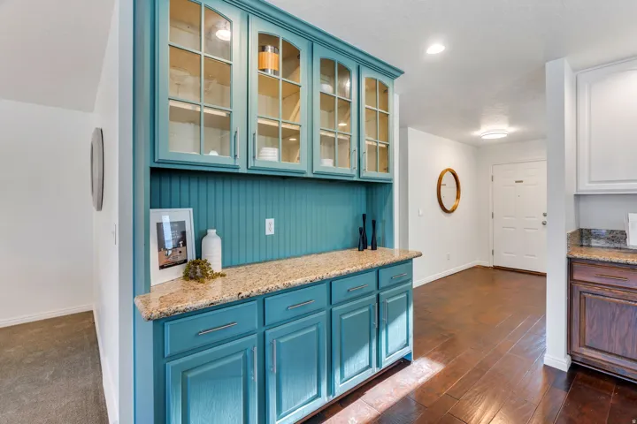 Kitchen featuring blue cabinets, light stone counters, and glass fronted cabinets