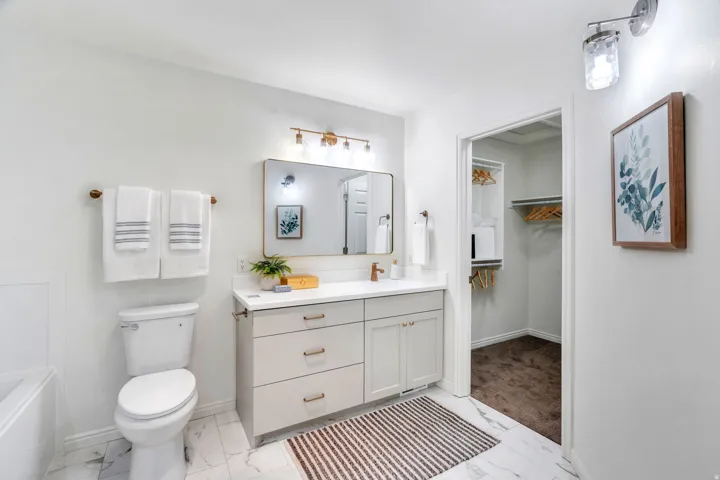 Primary suite Full bath featuring vanity, light marble finish floors, and a walk in closet
