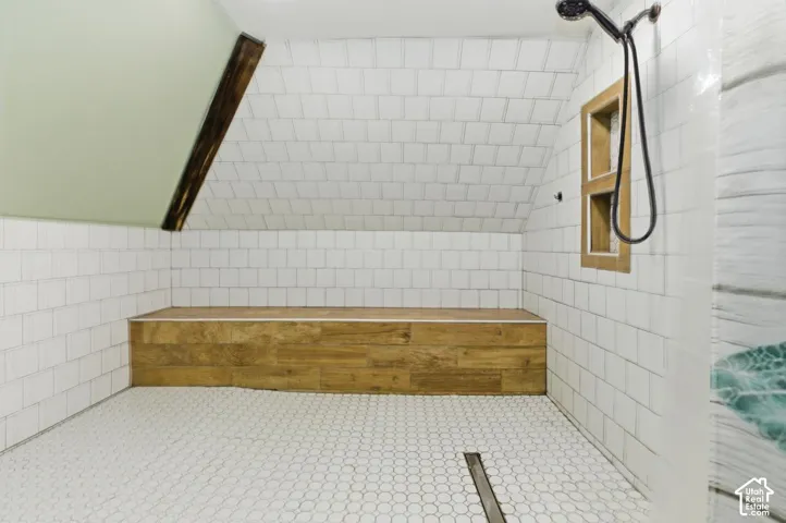 Full bathroom with tile walls, a tile shower, and lofted ceiling