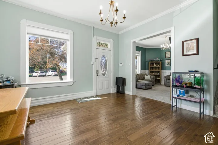Entrance foyer with suspended lighting, crown molding, and dark wood-style flooring