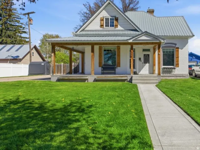 View of front facade featuring covered porch, a front yard, a chimney, and a standing seam roof