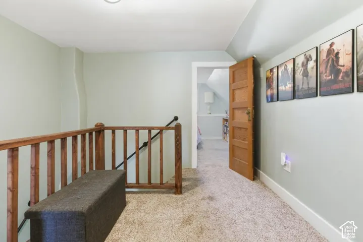Corridor with an upstairs landing, carpet flooring, and lofted ceiling