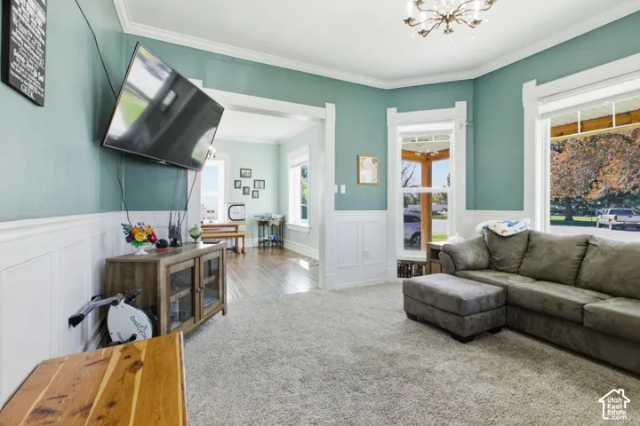 Living room featuring wainscoting, suspended lighting, a decorative wall, carpet floors, and ornamental molding