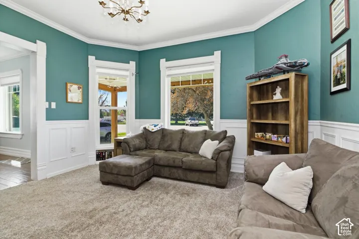 Carpeted living area with suspended lighting, a wainscoted wall, a decorative wall, and ornamental molding