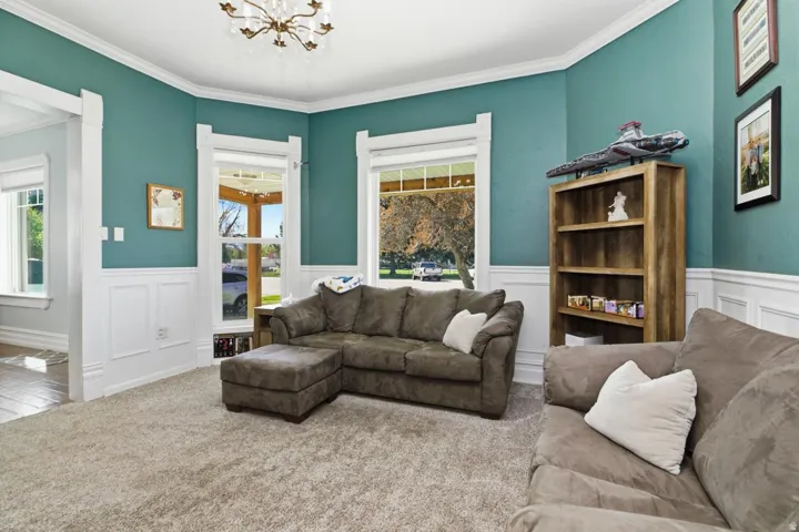 Carpeted living area with suspended lighting, a wainscoted wall, a decorative wall, and ornamental molding