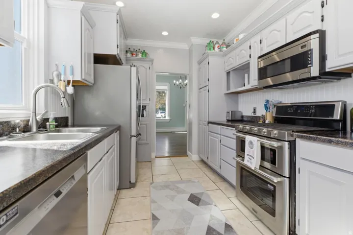 Kitchen featuring dark countertops, stainless steel appliances, crown molding, white cabinetry, and suspended lighting