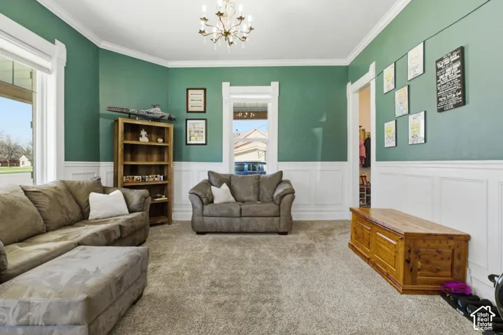 Living area featuring suspended lighting, crown molding, carpet, and wainscoting