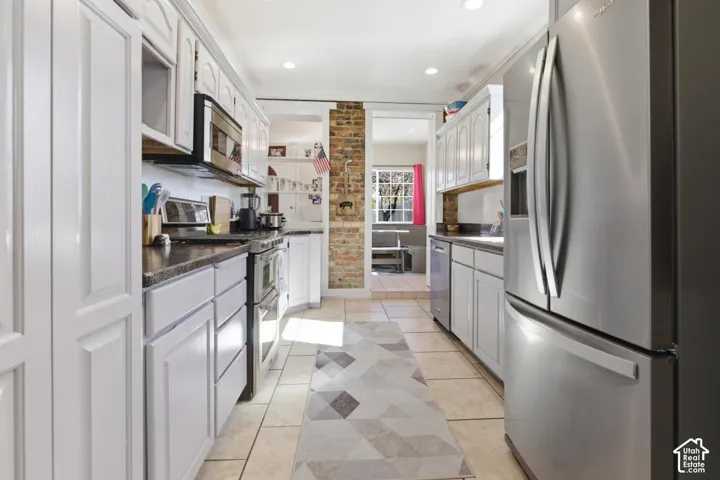 Kitchen featuring stainless steel appliances, light tile patterned floors, white cabinets, dark countertops, and recessed lighting