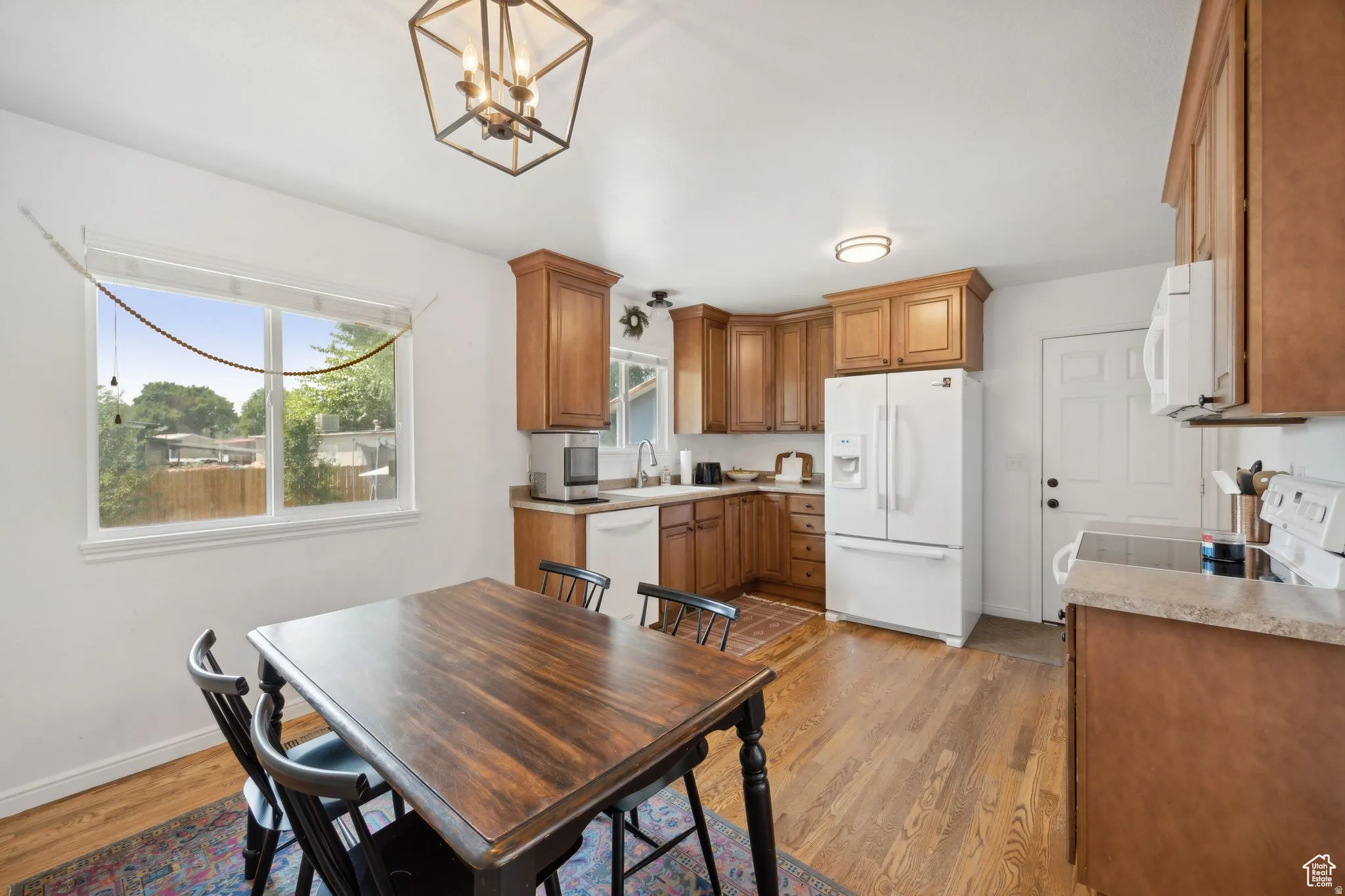 Kitchen with wood finish cabinetry, white appliances, light wood-type flooring, a chandelier, and light countertops