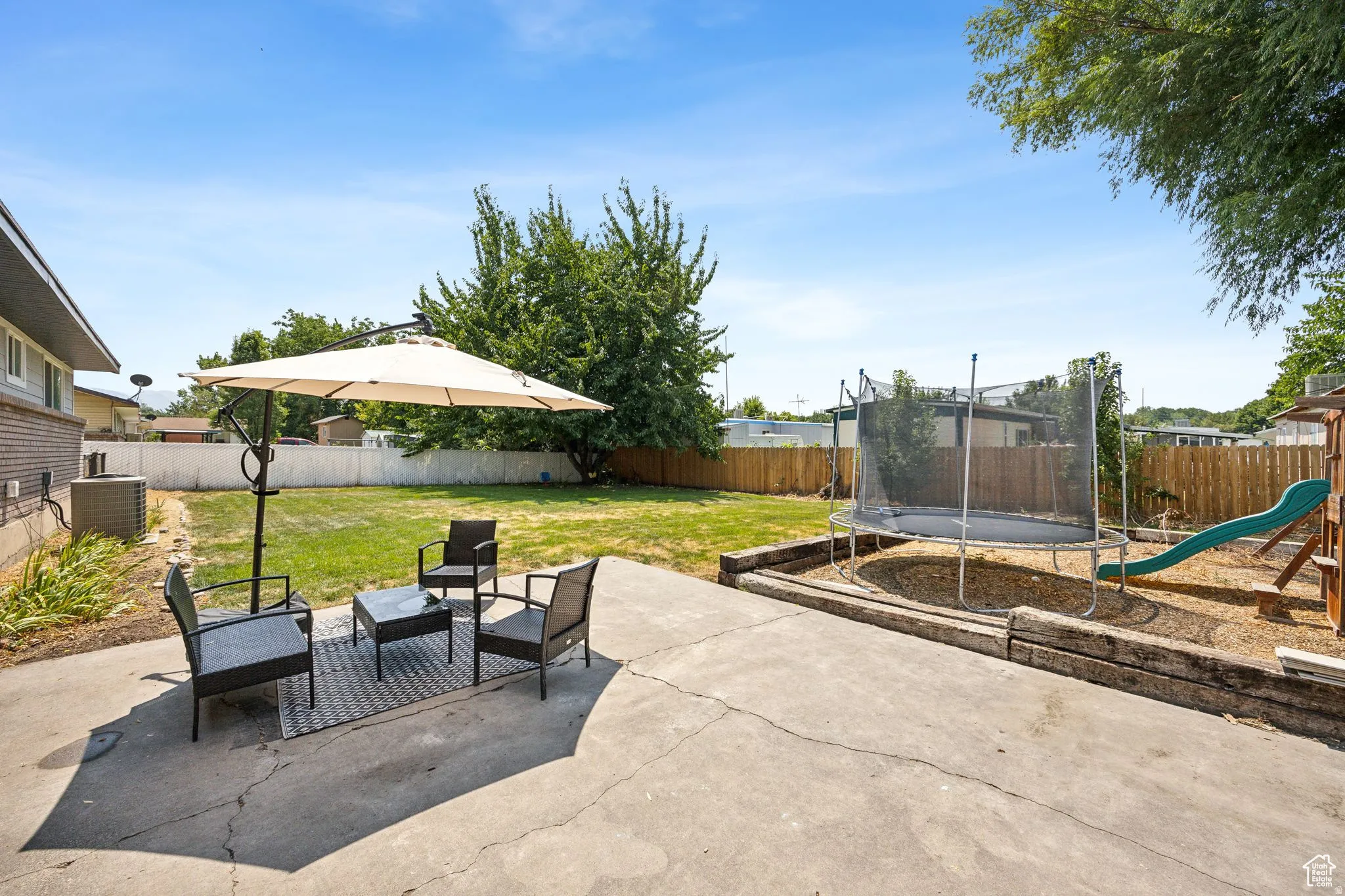 Fenced backyard with a patio, a trampoline, a playground, and outdoor furniture