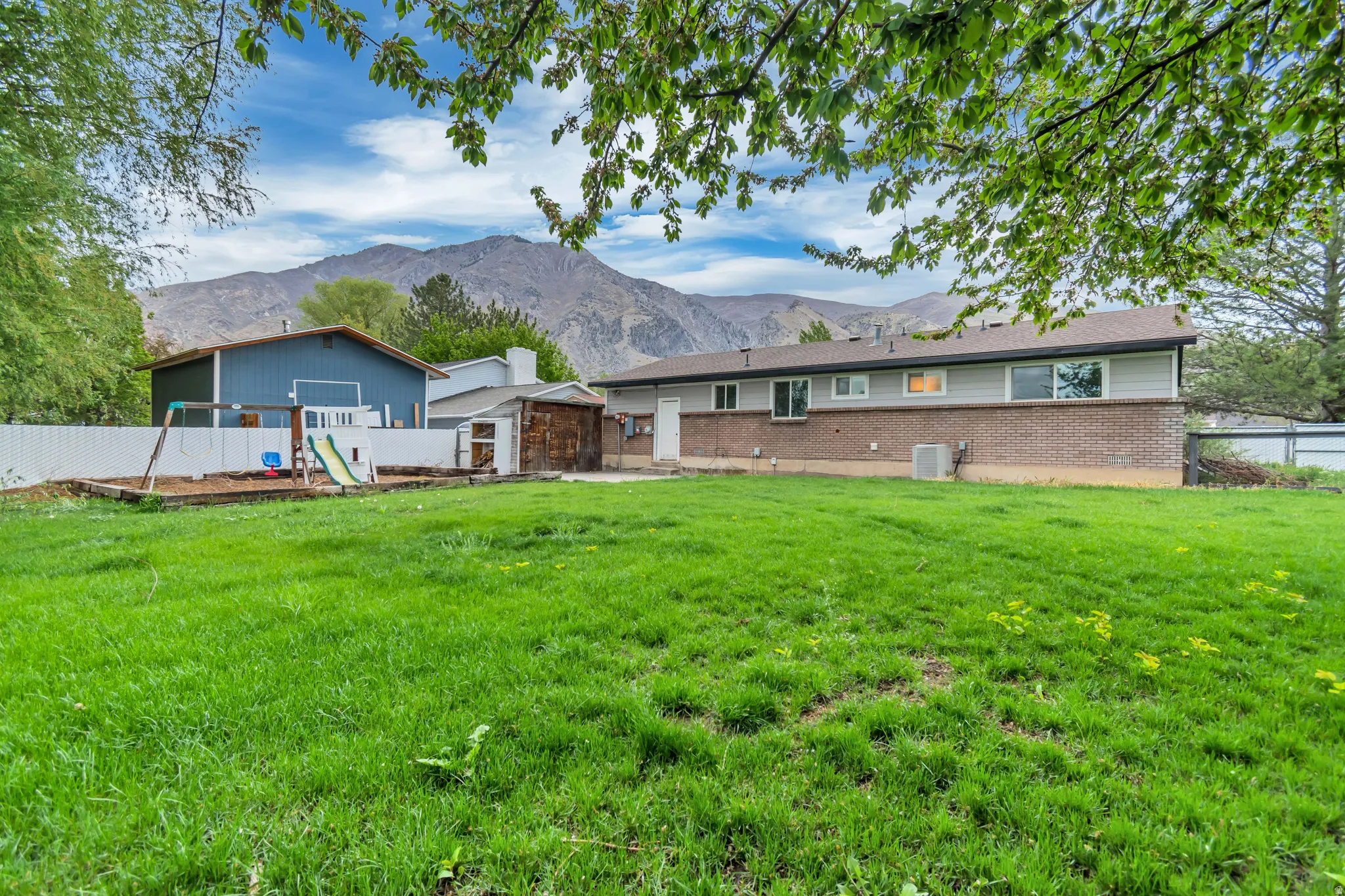 Rear view of property with a playground, a fenced backyard, a mountain view, and brick siding