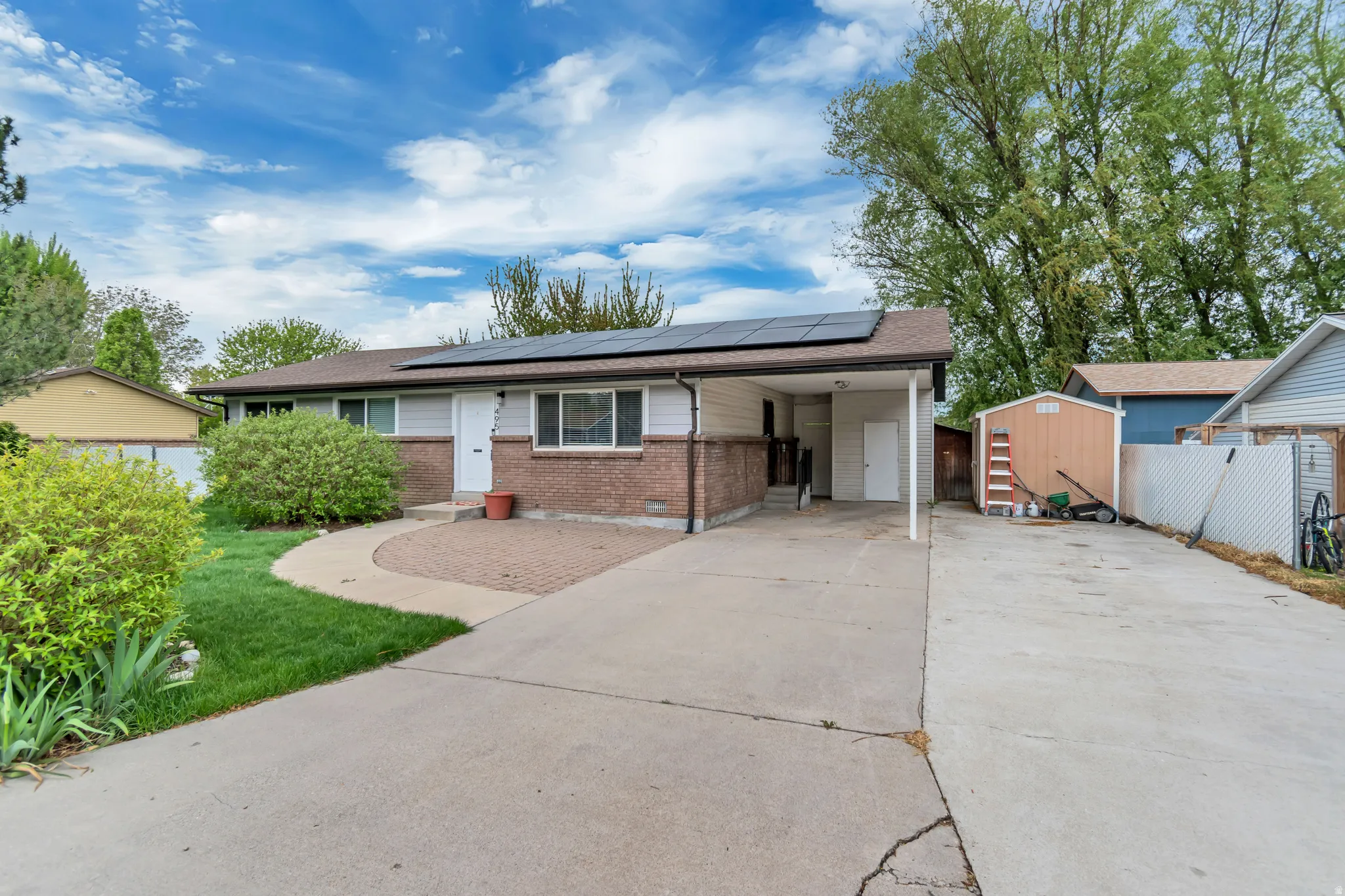 Ranch-style house featuring concrete driveway, roof mounted solar panels, brick siding, a carport, and a storage unit
