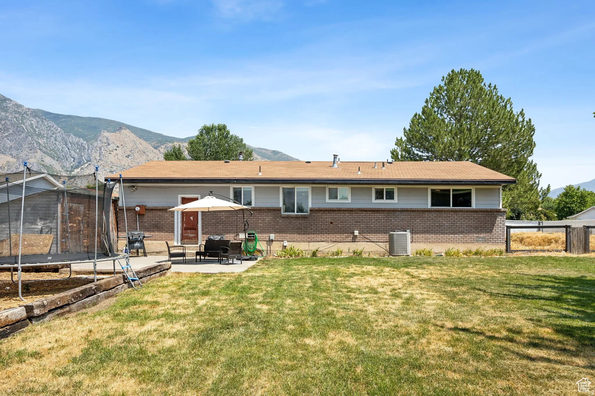Back of property featuring a trampoline, brick siding, a mountain view, a fenced backyard, and a patio area