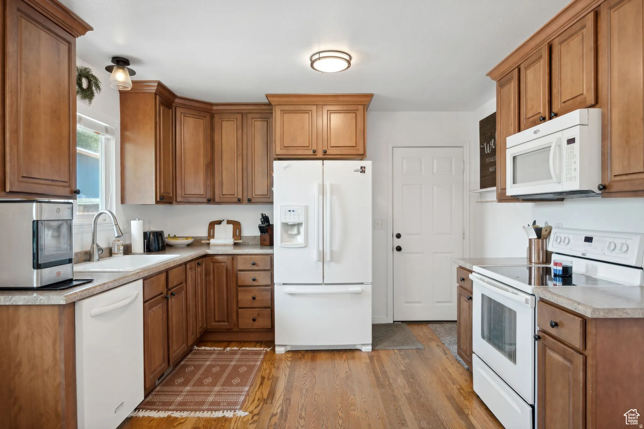 Kitchen featuring white appliances, wood finish cabinets, light countertops, and light wood finished floors