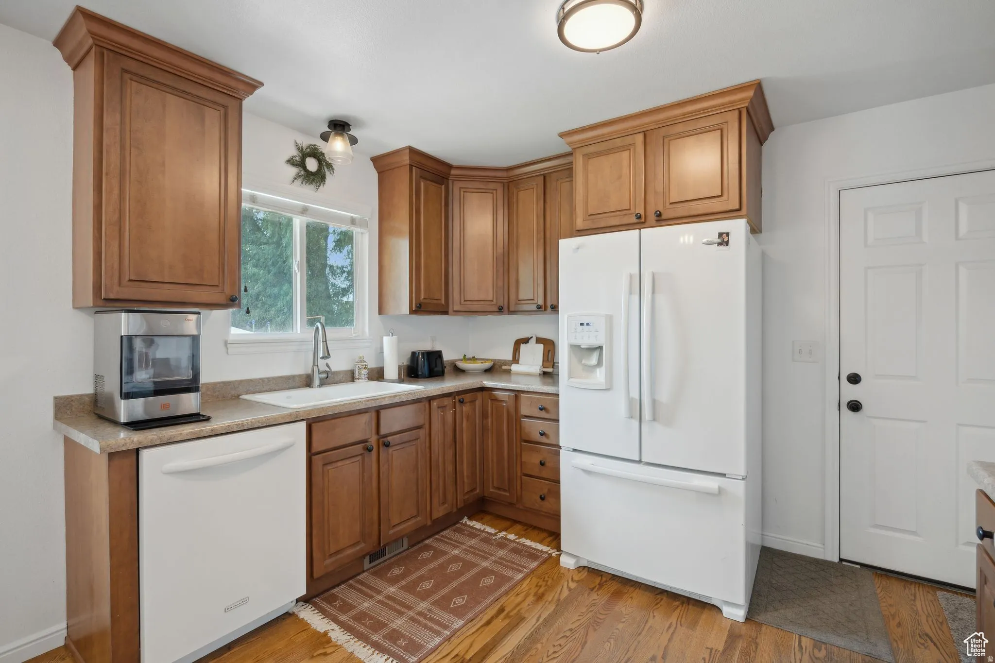 Kitchen featuring white appliances, wood finish cabinets, light countertops, and light wood-style floors