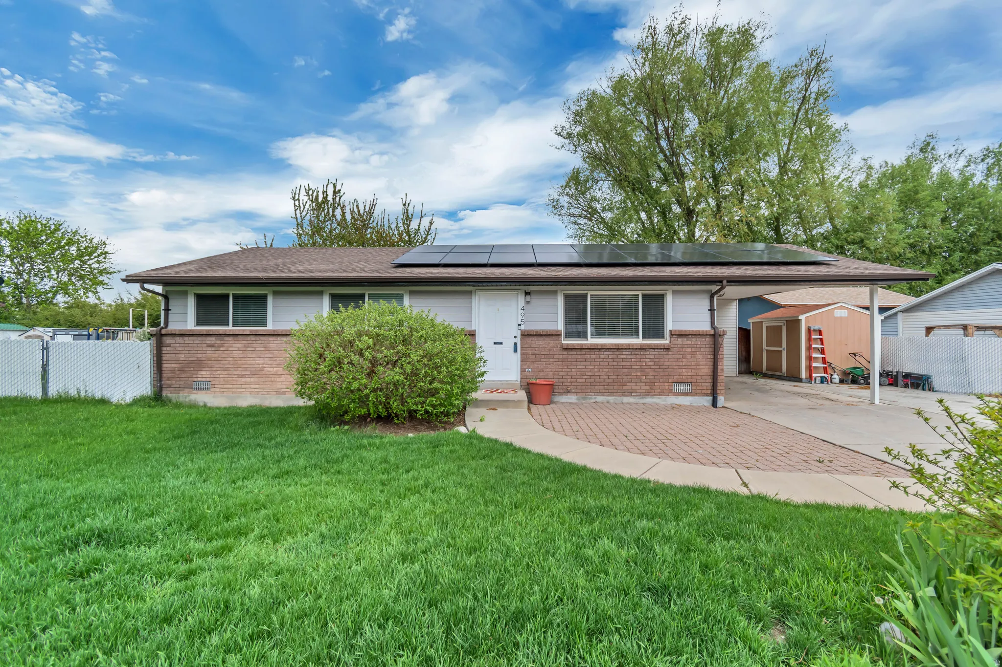 View of front of home with brick siding, solar panels, a storage unit, and a carport