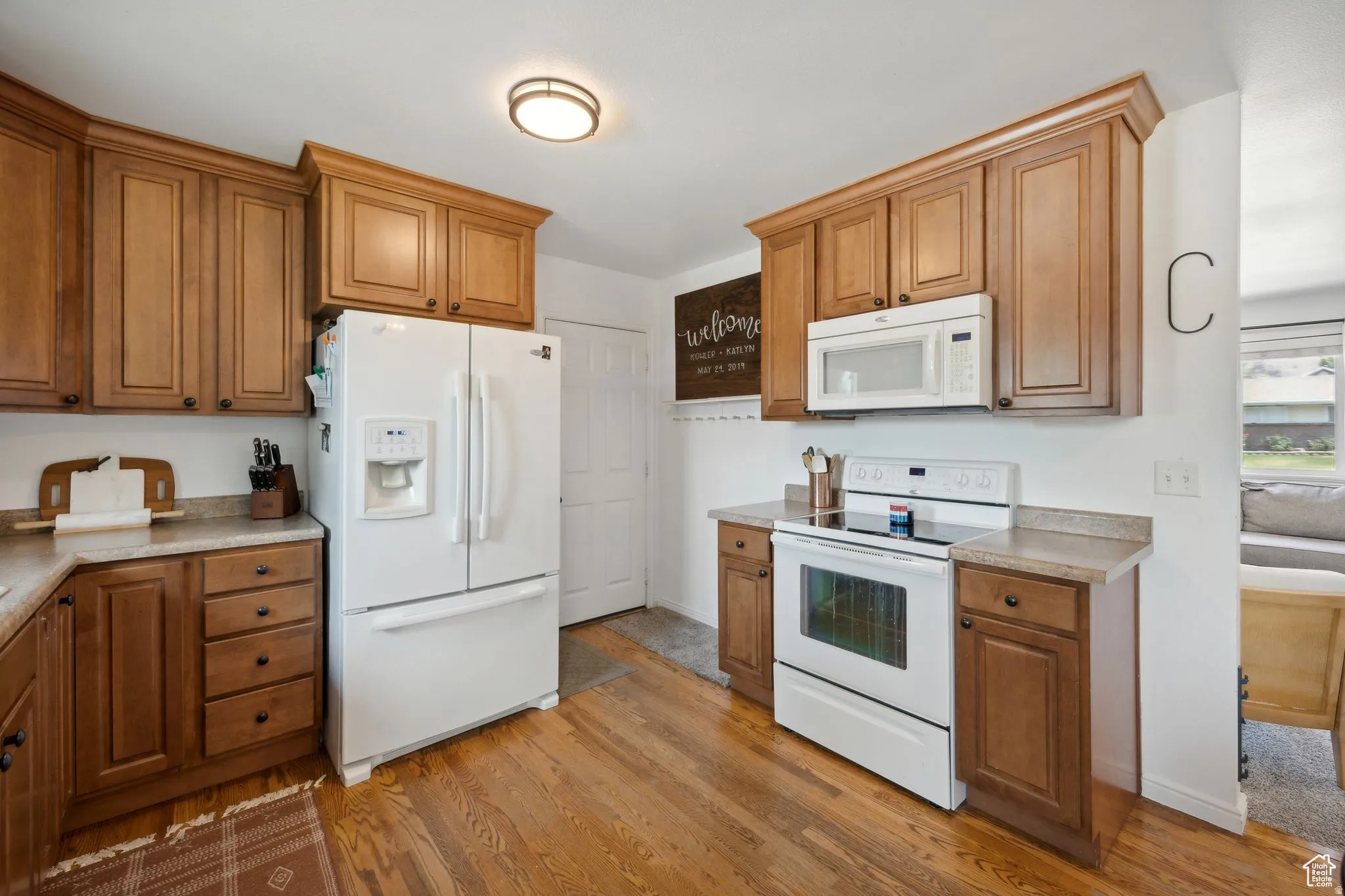 Kitchen with white appliances, light wood-style floors, wood finish cabinets, and light countertops