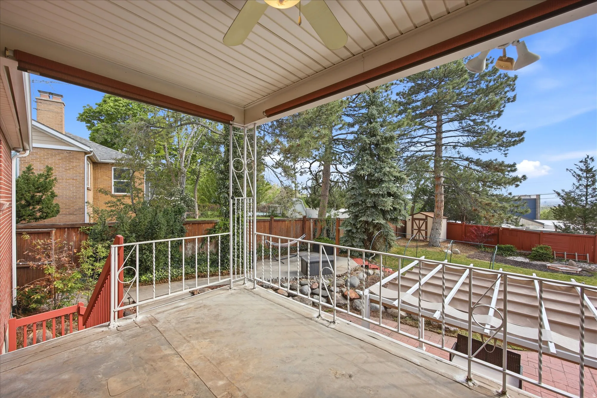 Covered porch featuring a fenced backyard, ceiling fan, and a storage unit