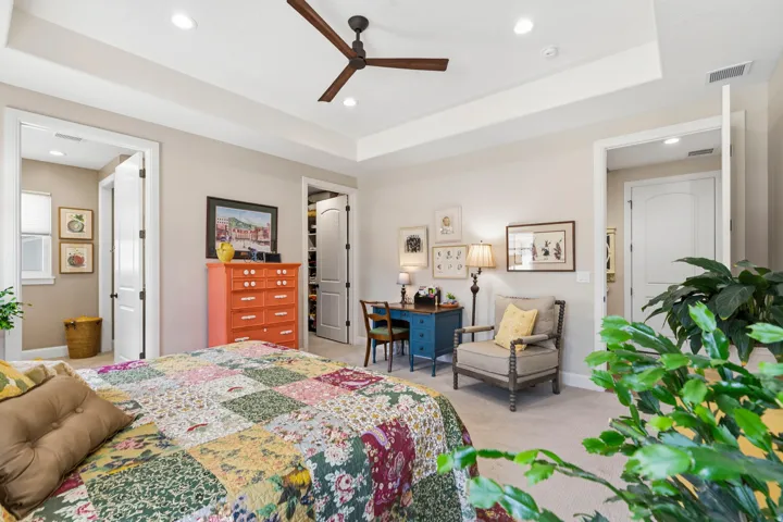 Bedroom with a raised ceiling, a walk in closet, recessed lighting, light carpet, and a ceiling fan